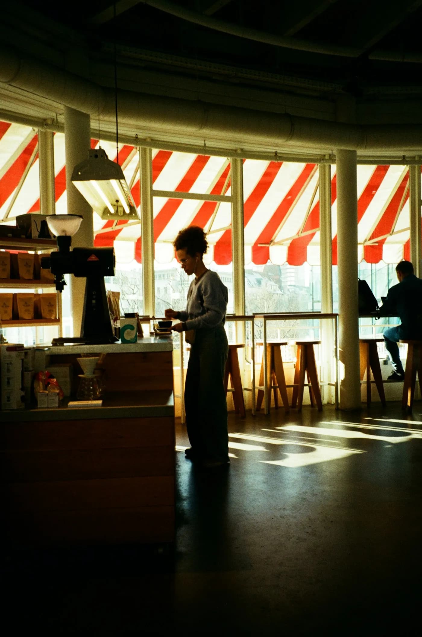 A barista behind the counter of a sunlit cafe, captured on film