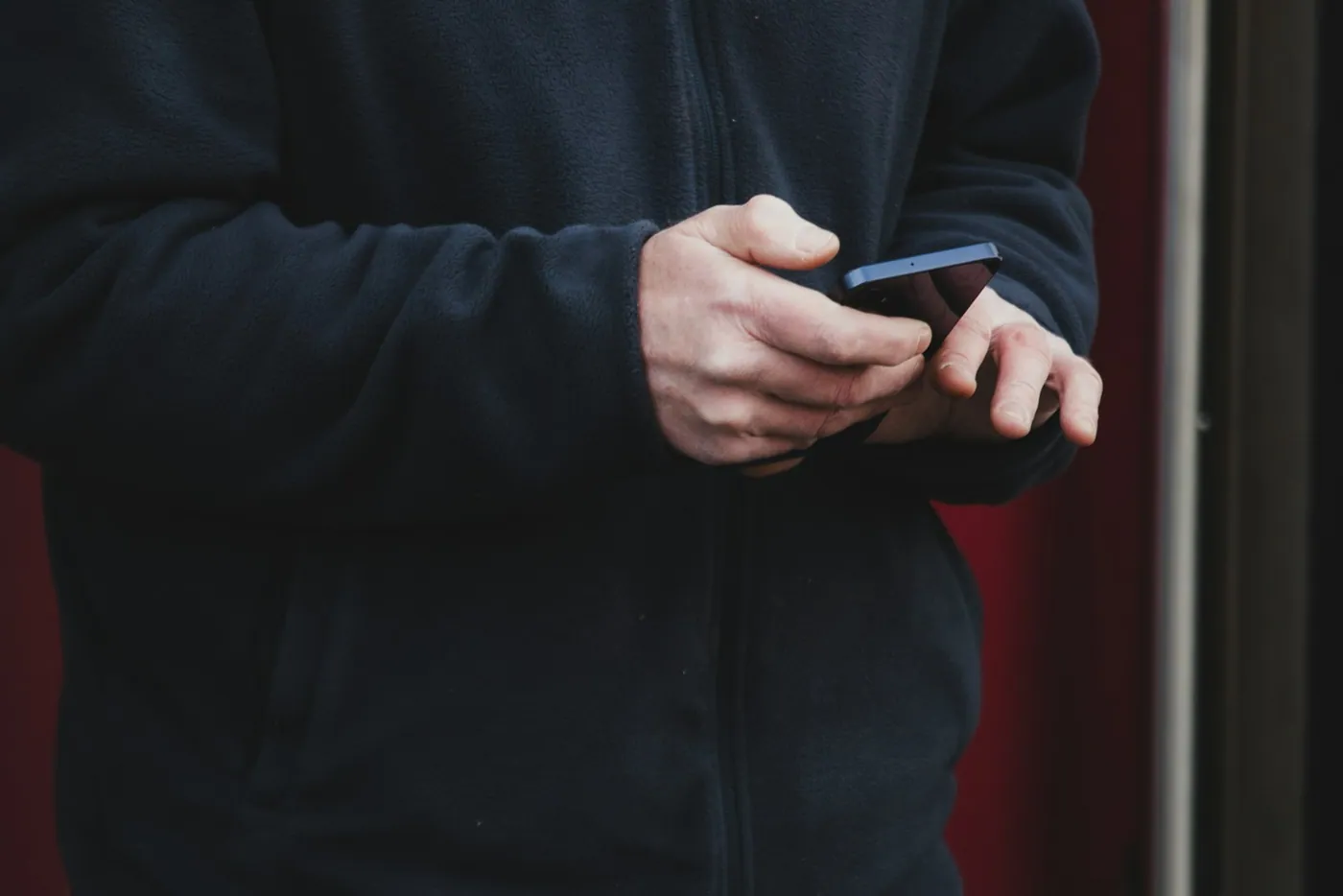 A person wearing a dark coat and using a smartphone with both hands
