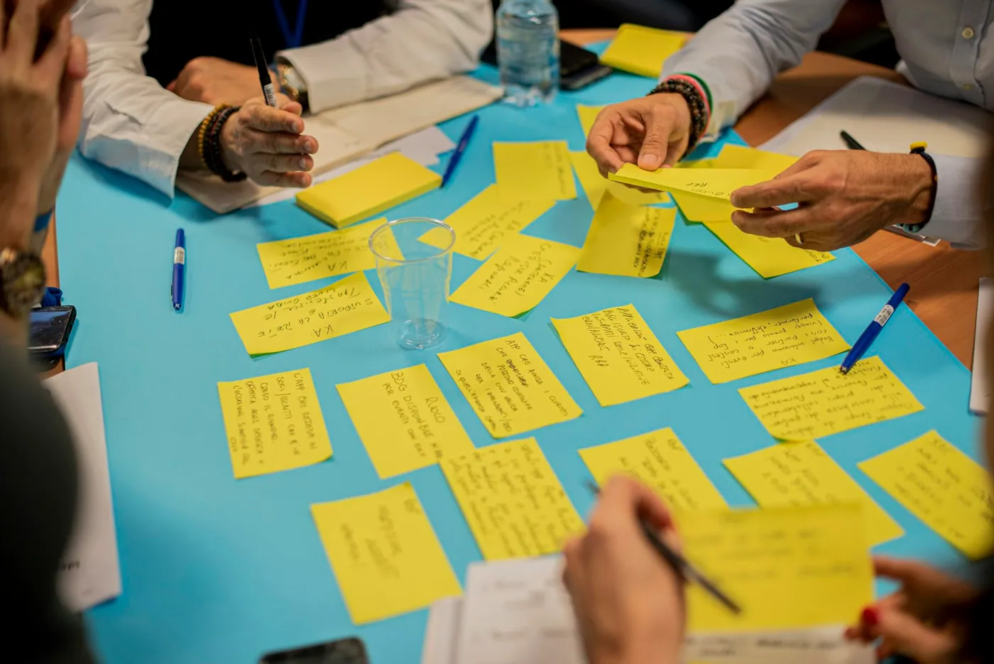 Workshop participants arranging handwritten sticky notes across a blue table