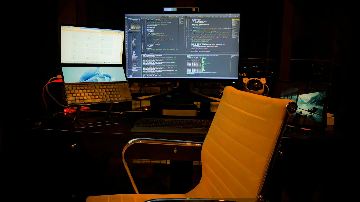 A real programming workspace with code on a monitor, a laptop and an office chair
